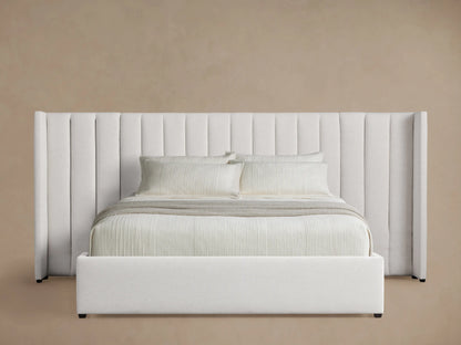 White Wyller bed with extended, channel-stitched headboard, low footboard, and white bedding, angled on a wood floor.