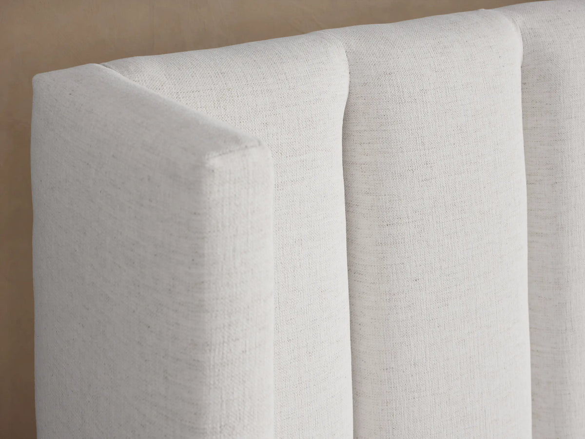 White Wyller bed with a tall, channel-stitched extended headboard, low footboard, and textured white bedding.