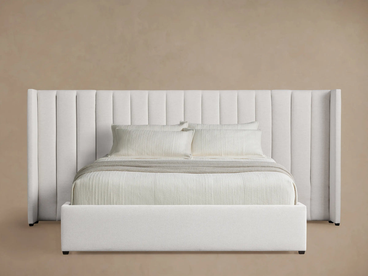 White Wyller Channel-Stitched Extended Headboard Bed with low footboard. Plush, vertically stitched headboard, white bedding, angled.