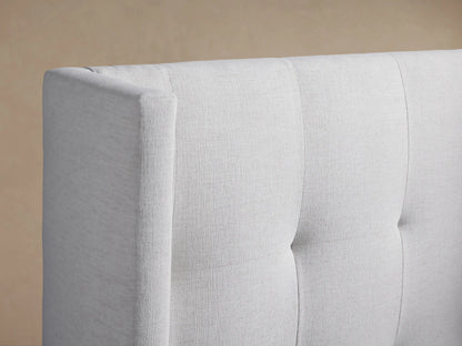 White Wyller Box-Tufted Twin Bed with a tall, winged box-tufted headboard and matching footboard, centered against a light brown wall.