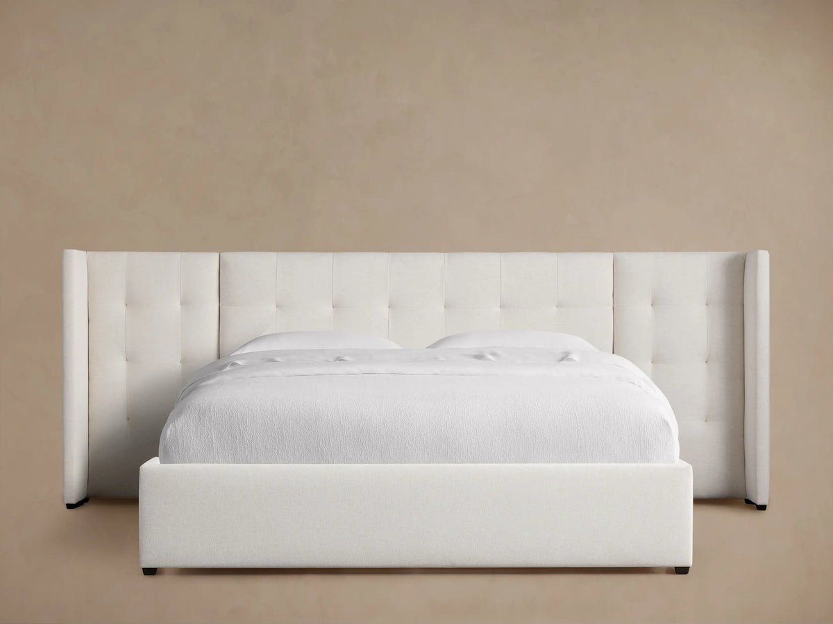 Wyller white box-tufted extended headboard bed with low footboard, in a room with tan walls and wood floor.
