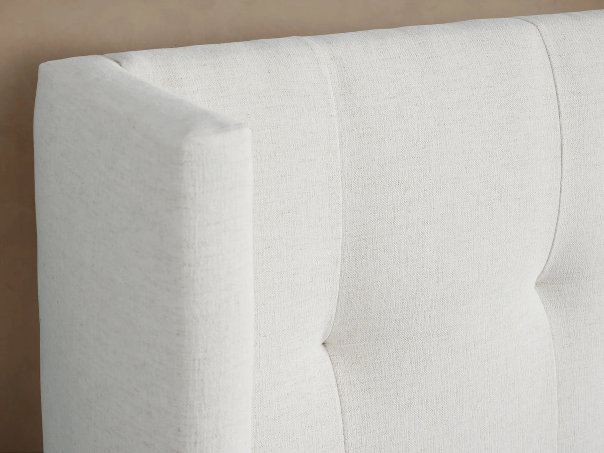 Wyller Box-Tufted Extended Headboard Bed with low footboard, upholstered in light cream fabric, centered on beige wall.