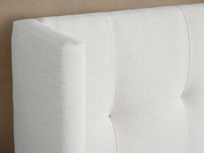 Wyller Box-Tufted Extended Headboard Bed with low footboard, upholstered in light cream fabric, centered on beige wall.