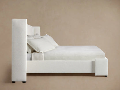 Close-up of Wyller extended headboard, showing light cream, textured, box-tufted fabric with vertical stitching & a side wing.