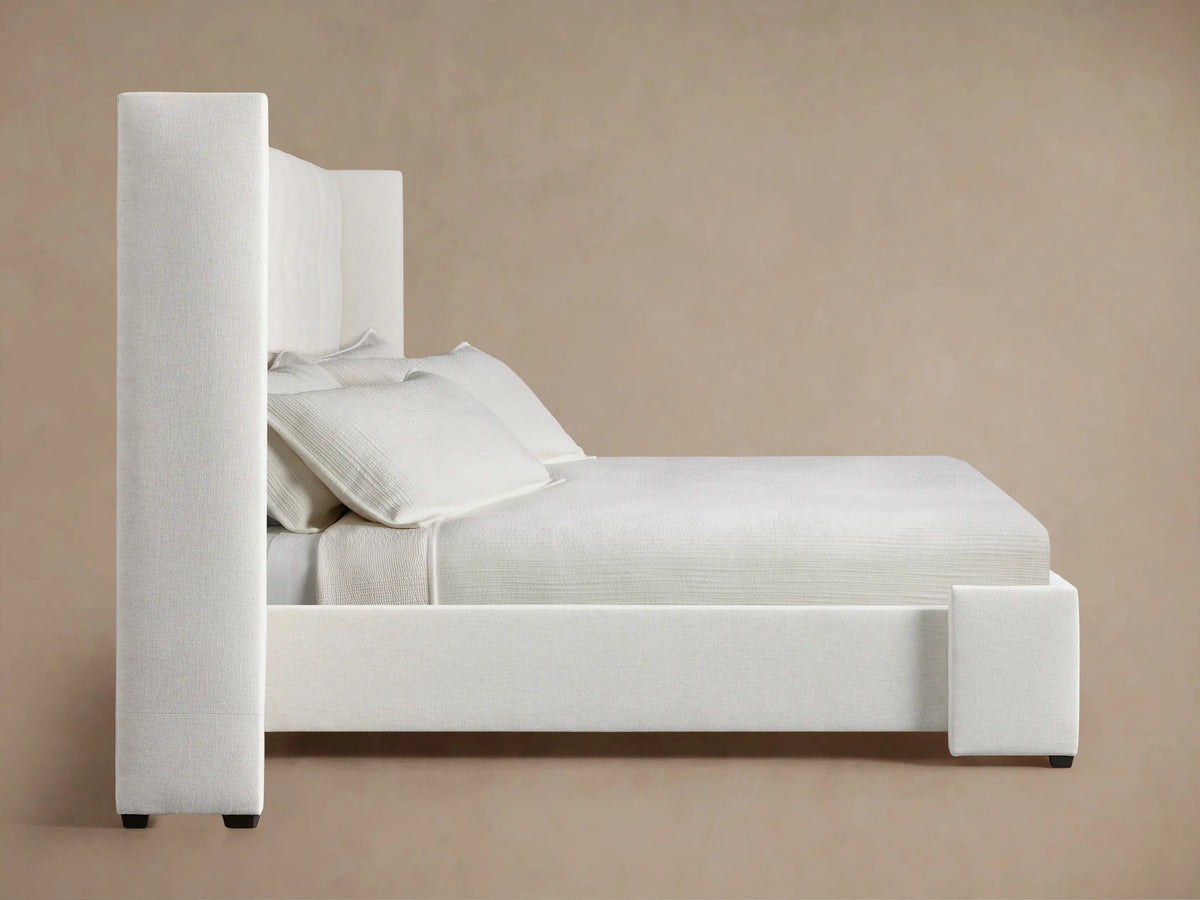 Close-up, angled view of Wyller Box-Tufted Extended Headboard in off-white textured fabric, with a side panel and a visible tuft.