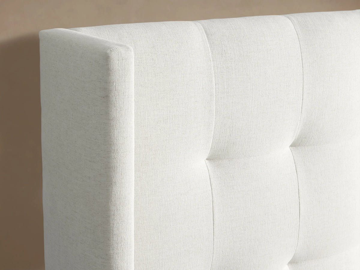 Wyller Box-Tufted Extended Headboard Bed, upholstered in white fabric, with a box-tufted headboard & low footboard, against a beige wall.