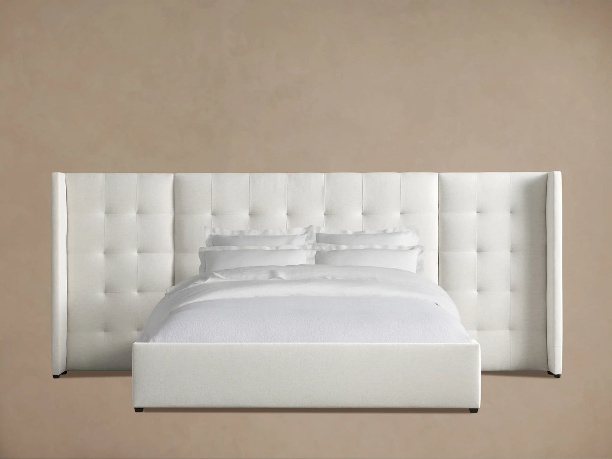 Wyller Box-Tufted Extended Headboard Bed, white upholstered, with low footboard, white bedding, against tan wall, wood floor.