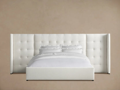 Wyller Box-Tufted Extended Headboard Bed, white upholstered, with low footboard, white bedding, against tan wall, wood floor.
