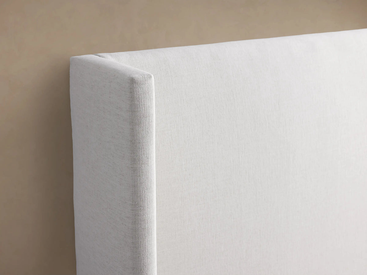 Wyller upholstered bed: extended white headboard with angled side panels, low footboard, white bedding.