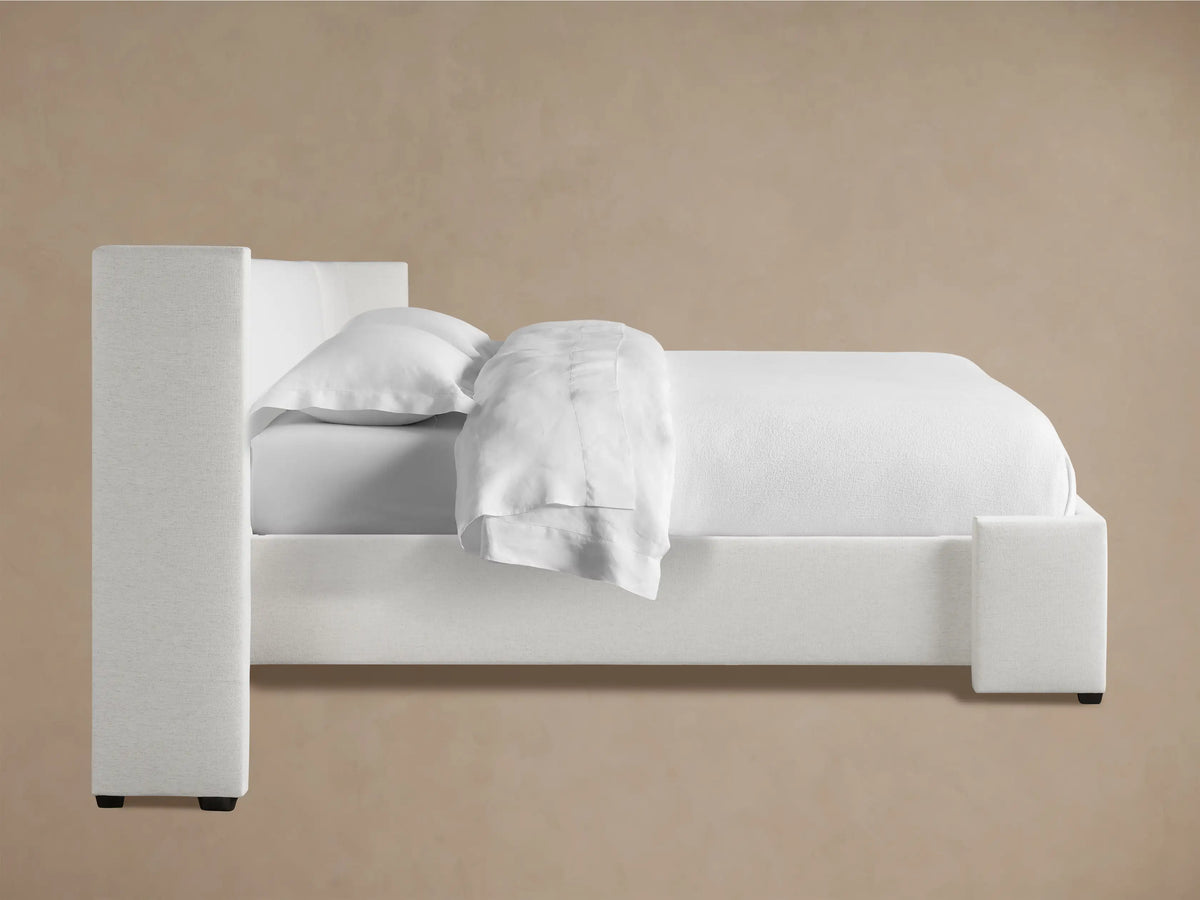 Close-up of Wyller Extended Headboard, upholstered in a light off-white textured fabric, showing a padded corner against a beige wall.