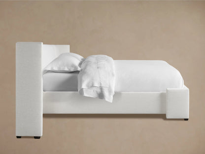 Close-up of Wyller Extended Headboard, upholstered in a light off-white textured fabric, showing a padded corner against a beige wall.