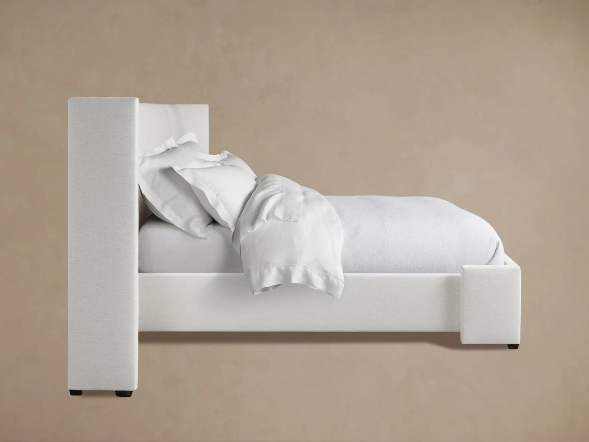 Close-up of the Wyller Extended Headboard Bed, showing the top left corner of the thick, textured light grey upholstered headboard against a beige wall.