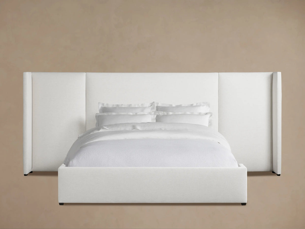 White Wyller Extended Headboard Bed with Low Footboard, upholstered, with white bedding, on wood floor against tan wall.
