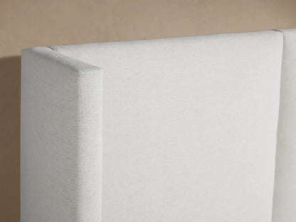 White upholstered Wyller Extended Headboard Bed, low footboard, with white bedding against a neutral wall.