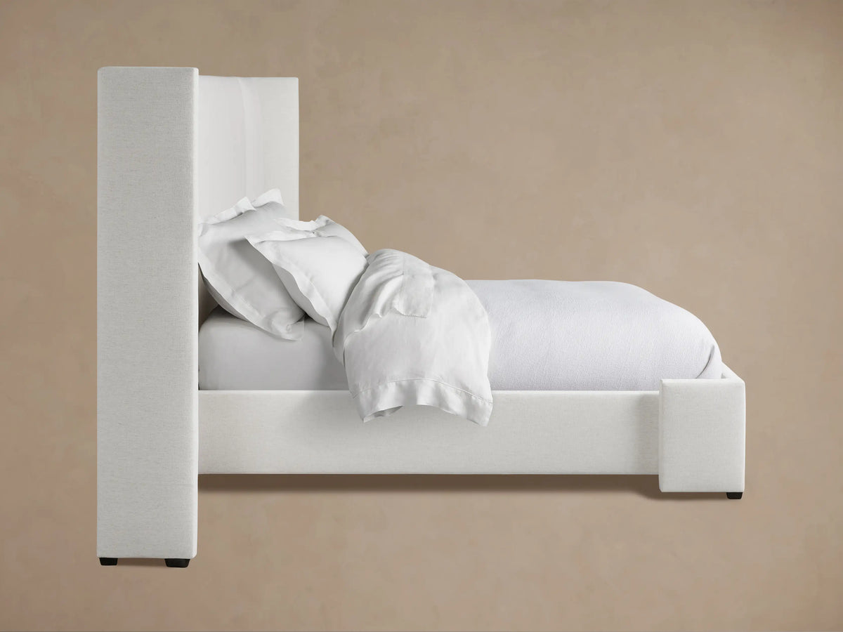 Wyller Extended Headboard Bed with light grey textured fabric. Close-up of the wingback corner against a warm beige wall.