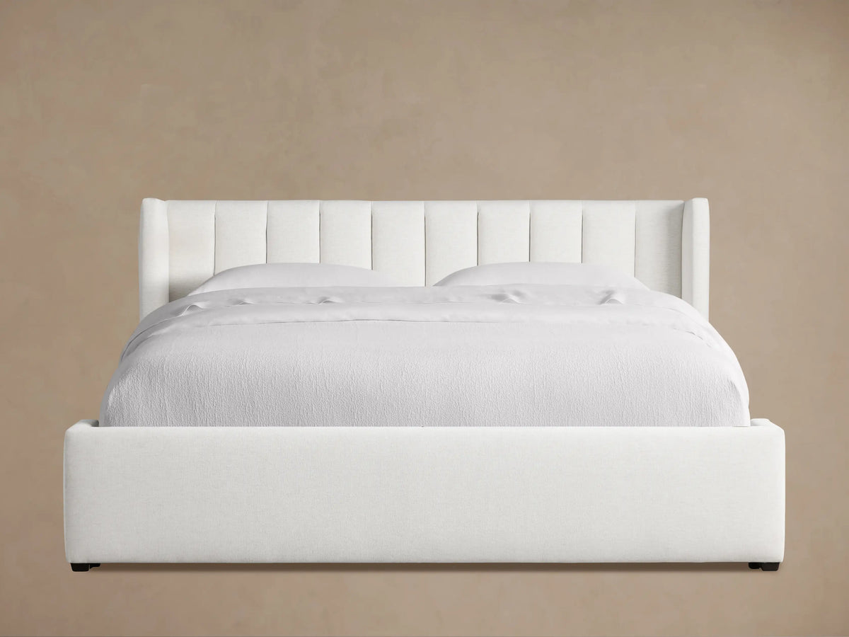 White Wyller Channel-Stitched Bed, low footboard, white bedding, angled on wood floor against beige wall.