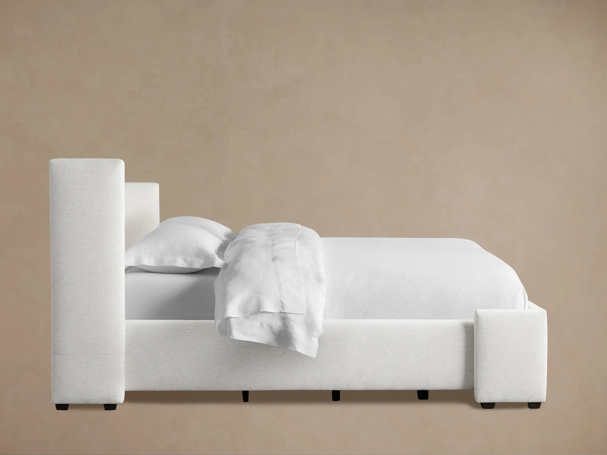 Close-up of Wyller Channel-Stitched Bed headboard. Light beige, textured fabric with plush vertical channels and soft corner.