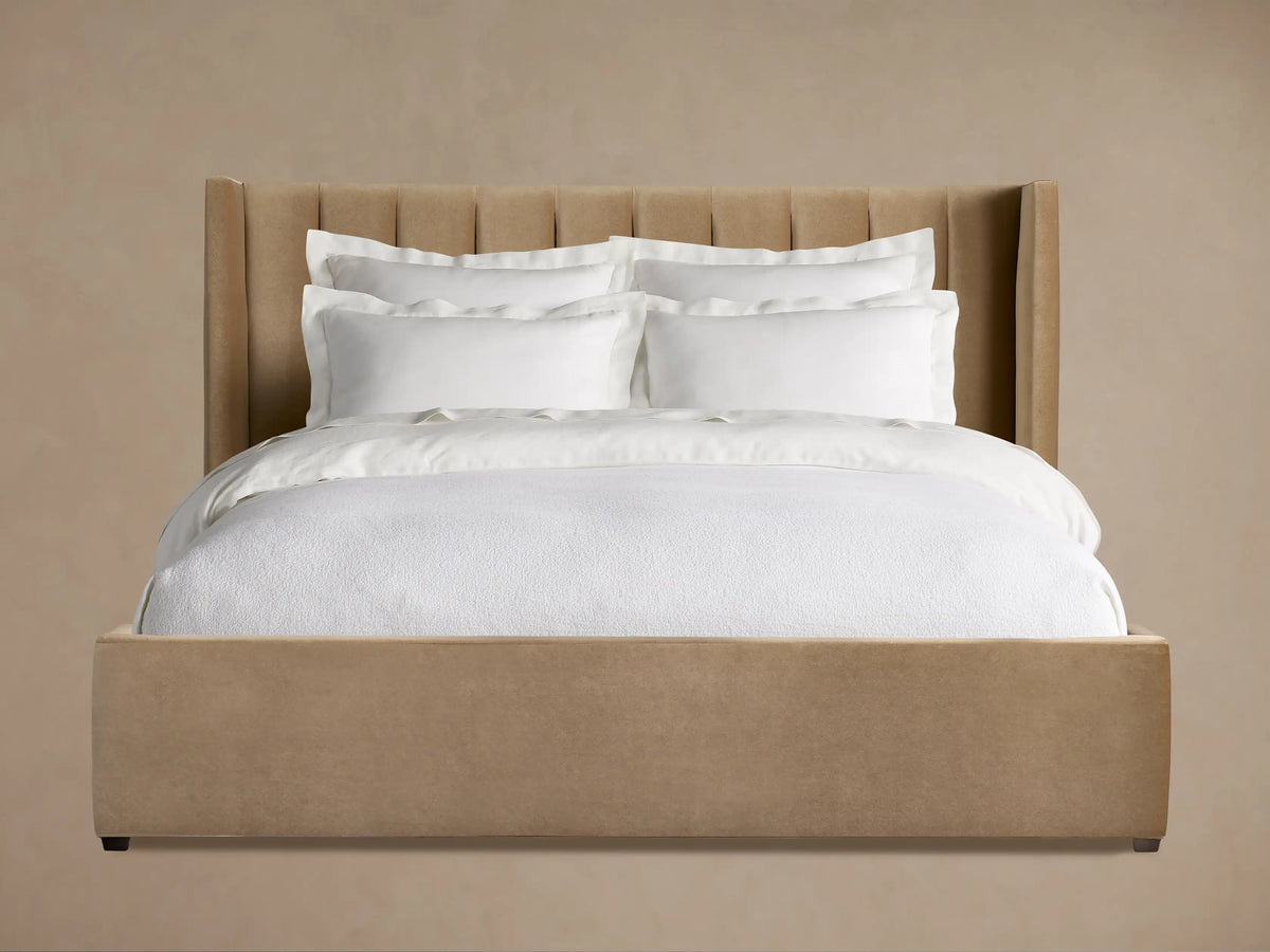 Wyller bed, tan upholstered with channel-stitched, winged headboard, low footboard, and crisp white bedding in a room.