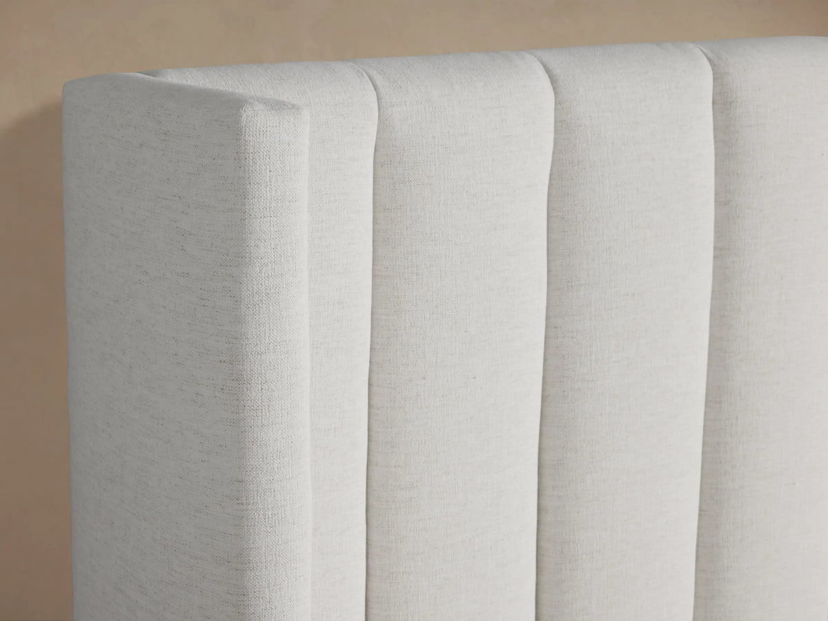 White Wyller Channel-Stitched Bed with a low footboard. Upholstered headboard has vertical channel stitching. Simple white bedding.