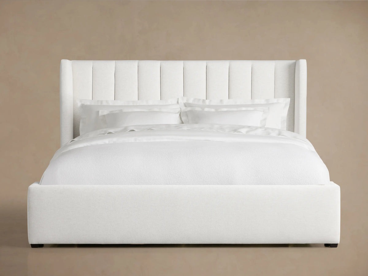 White Wyller Channel-Stitched Bed with tall, winged headboard, low footboard, & plush white bedding on wood floor.