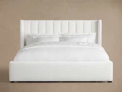 White Wyller Channel-Stitched Bed with tall, winged headboard, low footboard, & plush white bedding on wood floor.