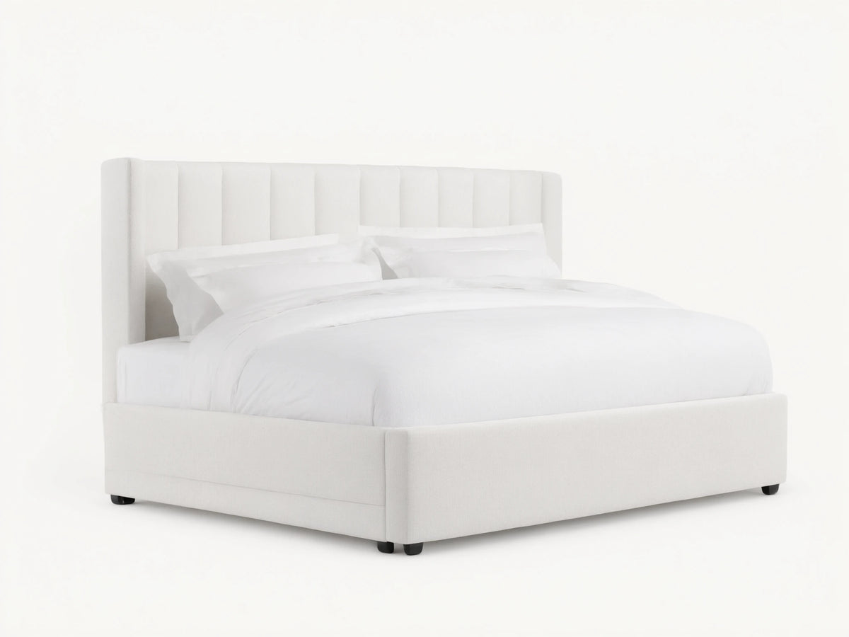 White Wyller Channel-Stitched Bed with tall, winged headboard, low footboard, & plush white bedding on wood floor.