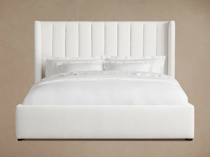 White upholstered Wyller Channel-Stitched Bed with a tall headboard, low footboard, and white bedding, angled in a room.