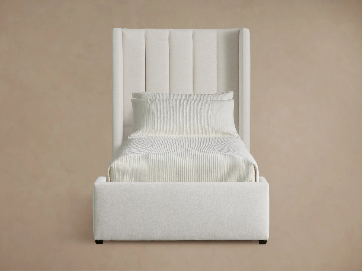White upholstered Wyller Channel-Stitched Twin Bed with channel-stitched headboard, pillows, and light bedding on a wooden floor.