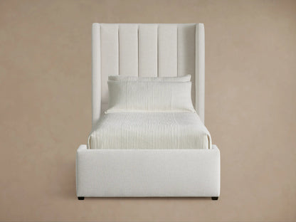 White upholstered Wyller Channel-Stitched Twin Bed with channel-stitched headboard, pillows, and light bedding on a wooden floor.