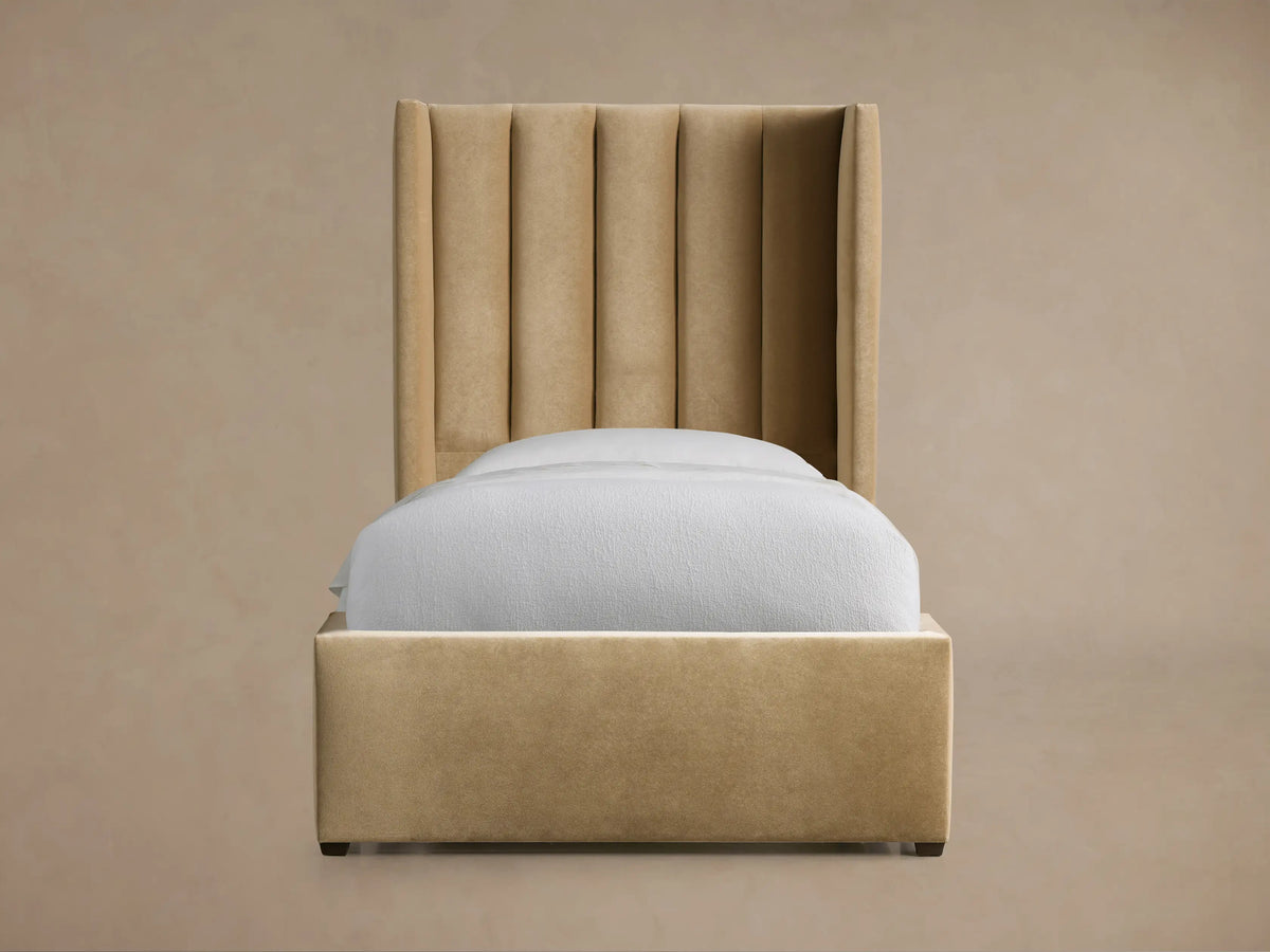 Tan Wyller Channel-Stitched Twin Bed with a tall, winged upholstered headboard, frame, and white bedding on a wood floor.