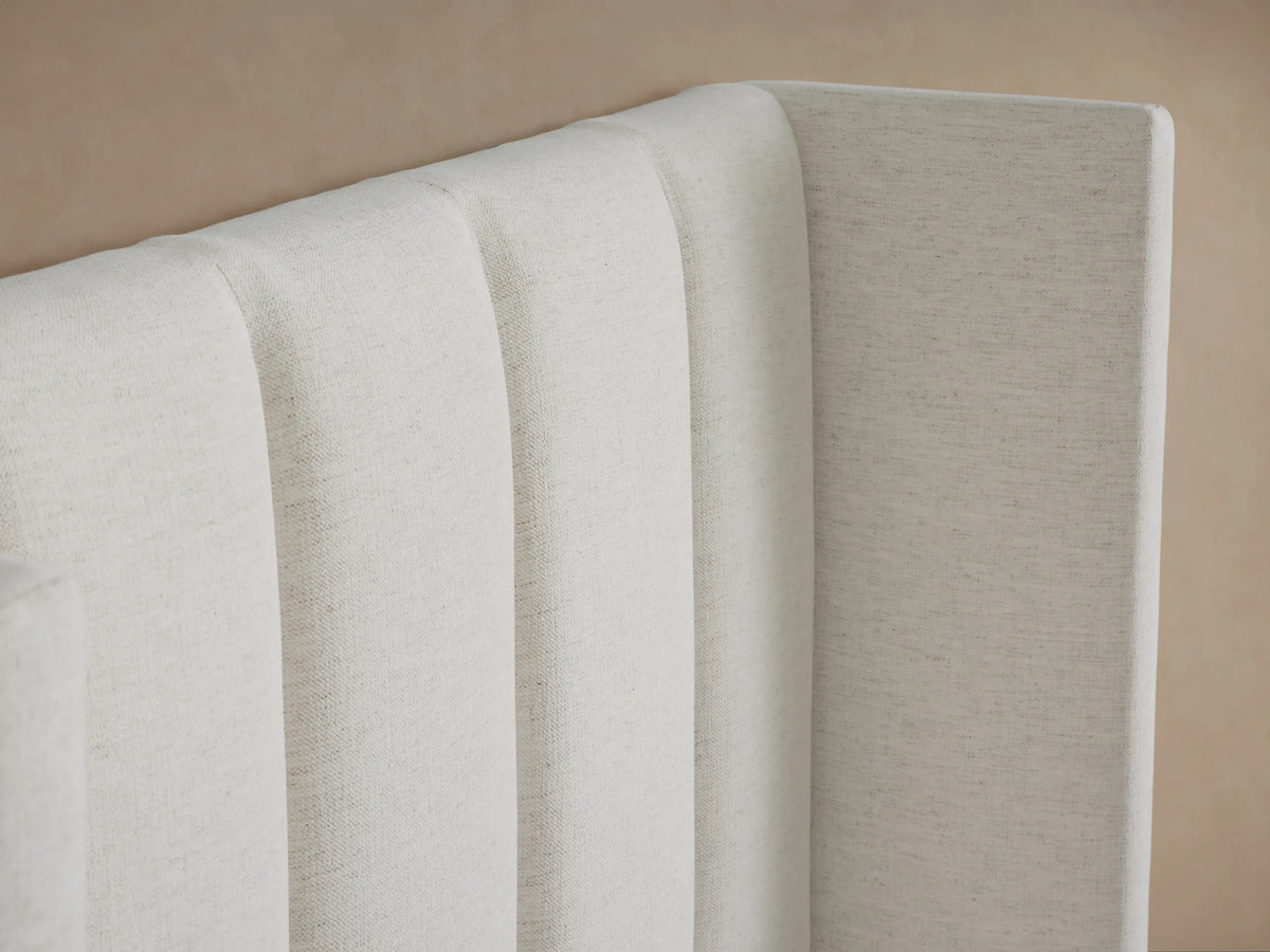 Light beige upholstered Wyller Channel-Stitched Twin Bed with a tall, vertically channel-stitched headboard, against a light brown wall.