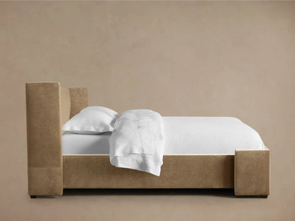 Side profile of a beige upholstered Wyller Bed with Low Headboard, featuring white bedding, a pillow, and folded duvet.