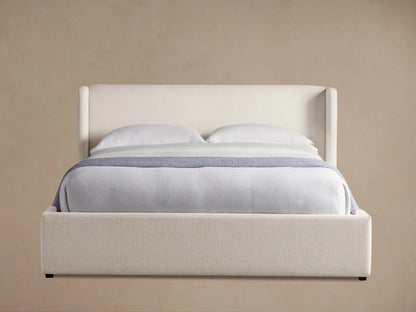 Wyller upholstered bed in light cream fabric, winged headboard, and platform base, with white bedding & blue throw.