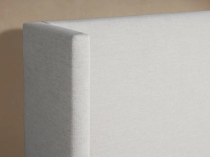 Close-up of Wyller Bed's light grey textured upholstered headboard, showing a clean top edge and slightly winged side.