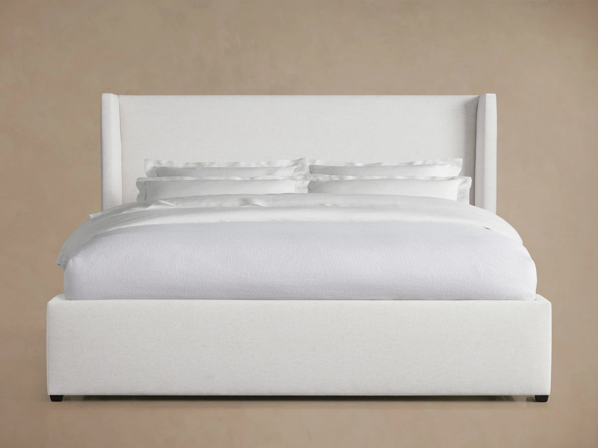 Wyller Bed with white upholstery, high wingback headboard, and plush bedding, set against a neutral background.