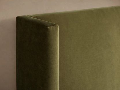 Front view of the green upholstered Wyller Bed with a winged headboard, made up with white quilted bedding and a light beige throw.