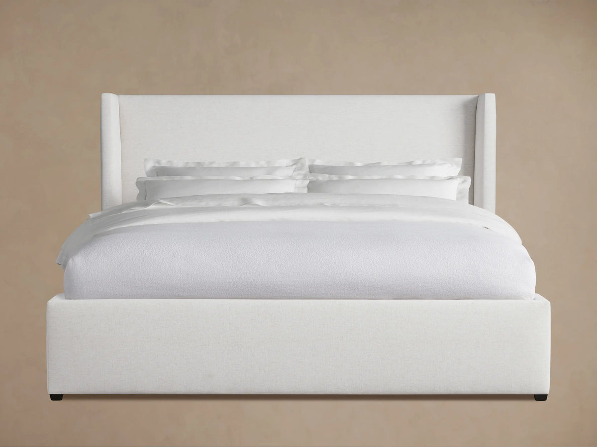 Wyller Bed: White upholstered bed with a tall, winged headboard, platform base, and white bedding, against a neutral wall.