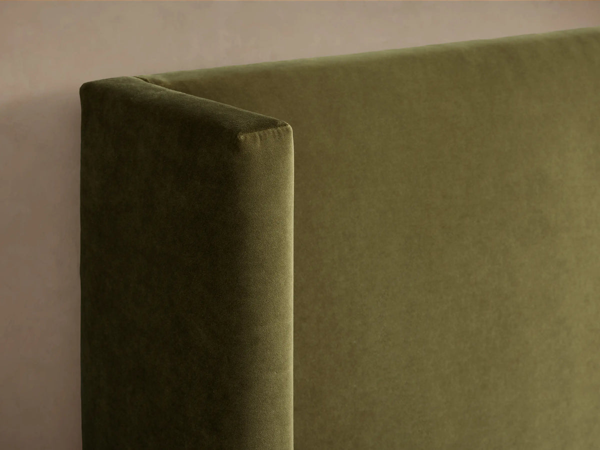 Front view of a green upholstered Wyller Bed with a tall headboard, made up with white quilted bedding and a light beige throw.