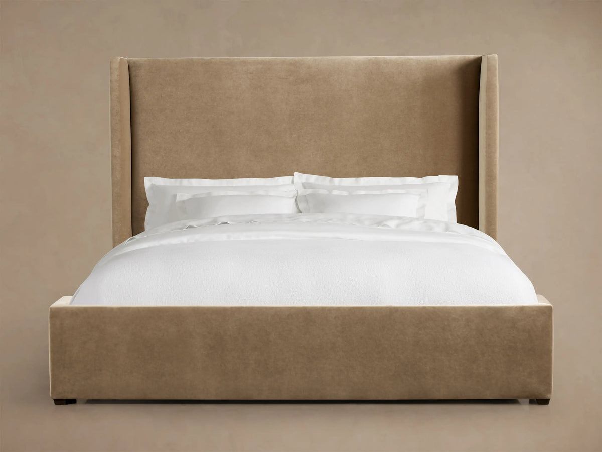Wyller Bed with a tall, light brown upholstered wingback headboard and matching frame, dressed with crisp white bedding.
