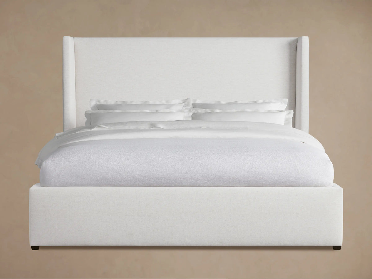Wyller Bed with white fabric upholstery, tall wingback headboard, and platform frame, dressed in white bedding, in a room.