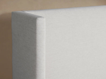 Wyller Bed with a tall, off-white upholstered headboard and base, dressed with crisp white bedding against a neutral wall.