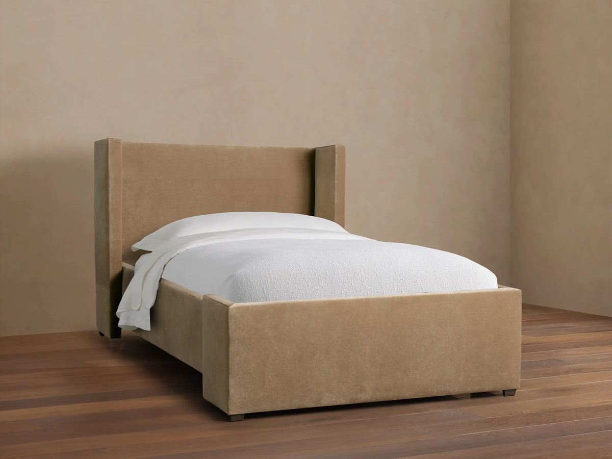 Wyller Twin Bed with light brown upholstered wingback headboard & frame, white mattress & bedding, on a dark wood floor.