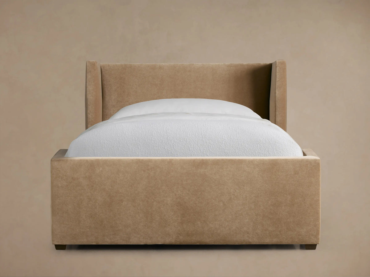 Wyller Twin Bed with light brown upholstered wingback headboard & frame, white mattress & bedding, on a dark wood floor.
