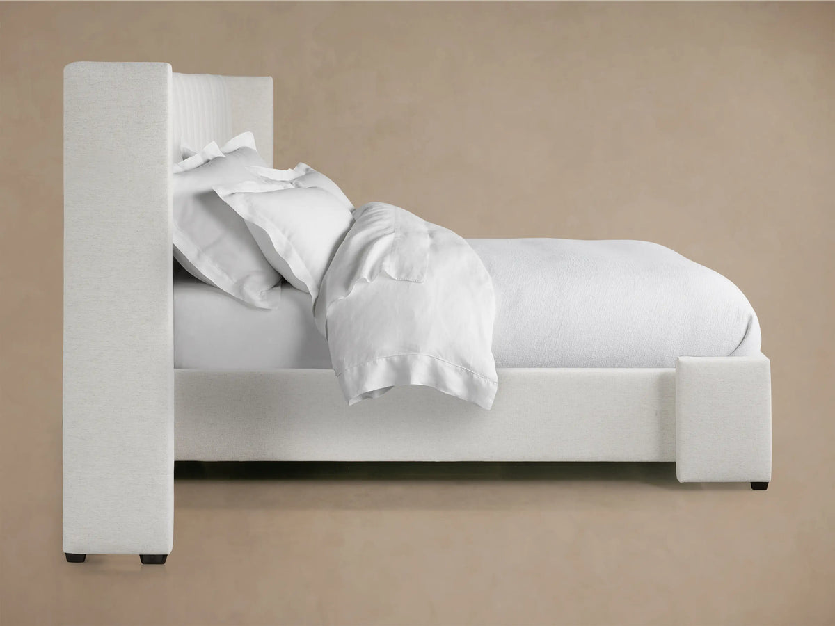 Wyller extended headboard close-up, upholstered in light cream textured fabric with vertical channel stitching.