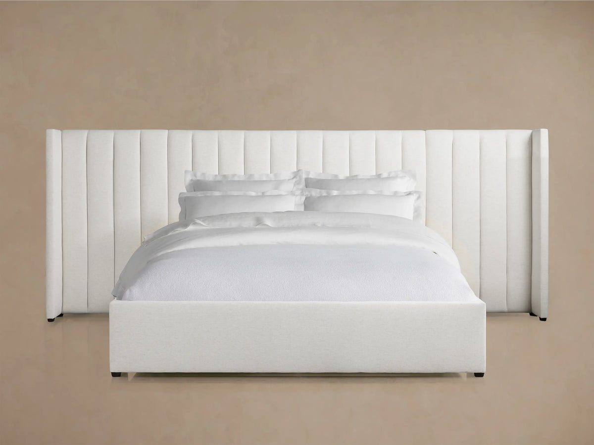 Wyller white channel-stitched extended headboard bed with a low footboard, dressed in white bedding, on a wooden floor.