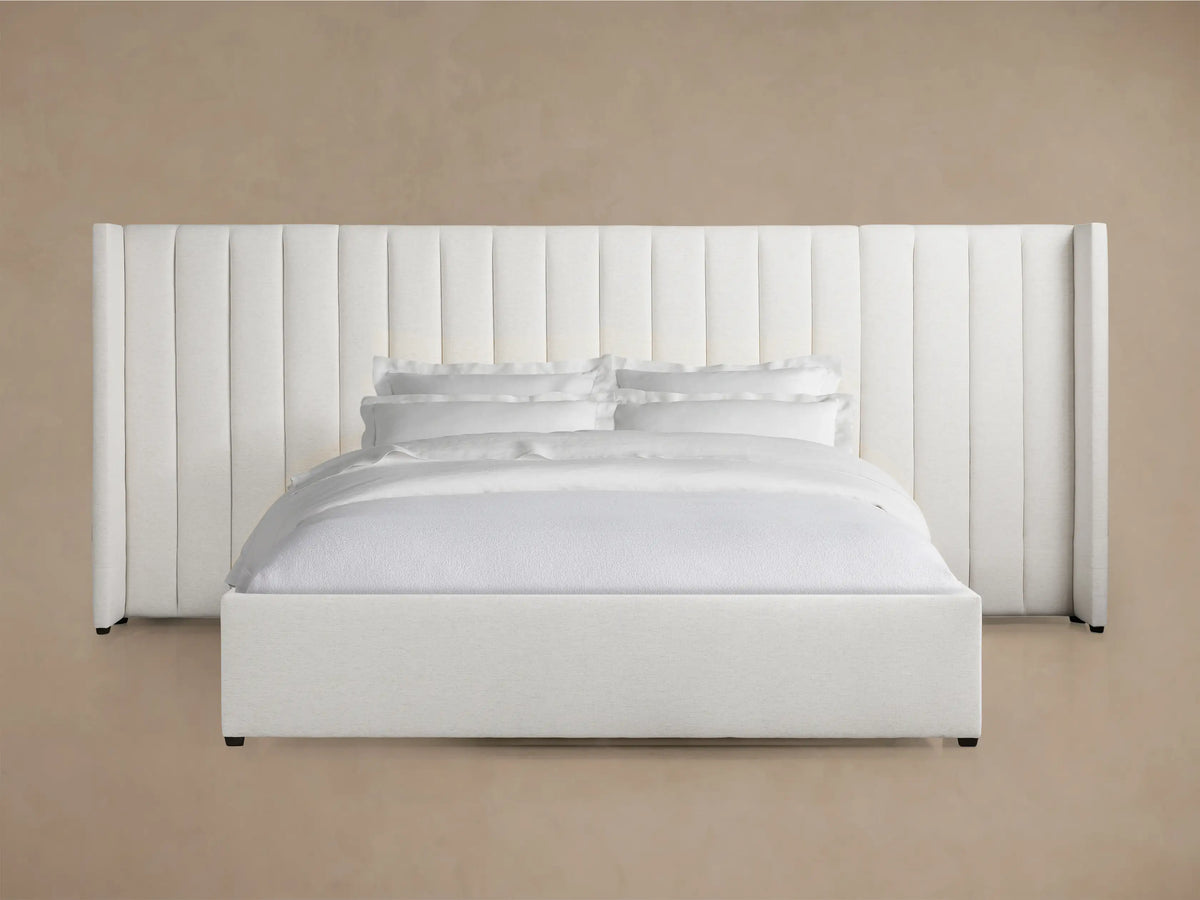 Wyller Channel-Stitched Extended Headboard Bed with Low Footboard. Light-colored fabric, white bedding, angled view.