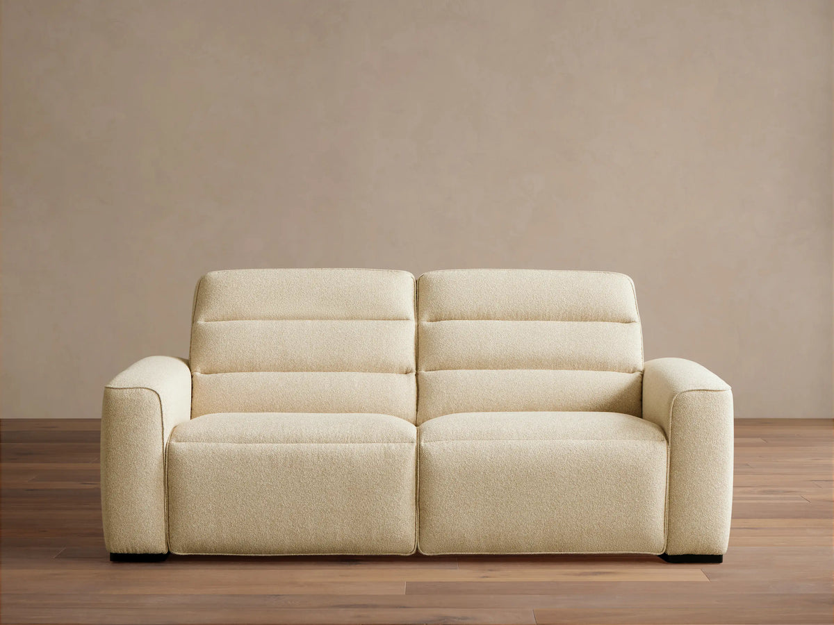 Front view of the cream Borough Two-Piece Motion Sofa, a two-seater with horizontally stitched back cushions and wide armrests.
