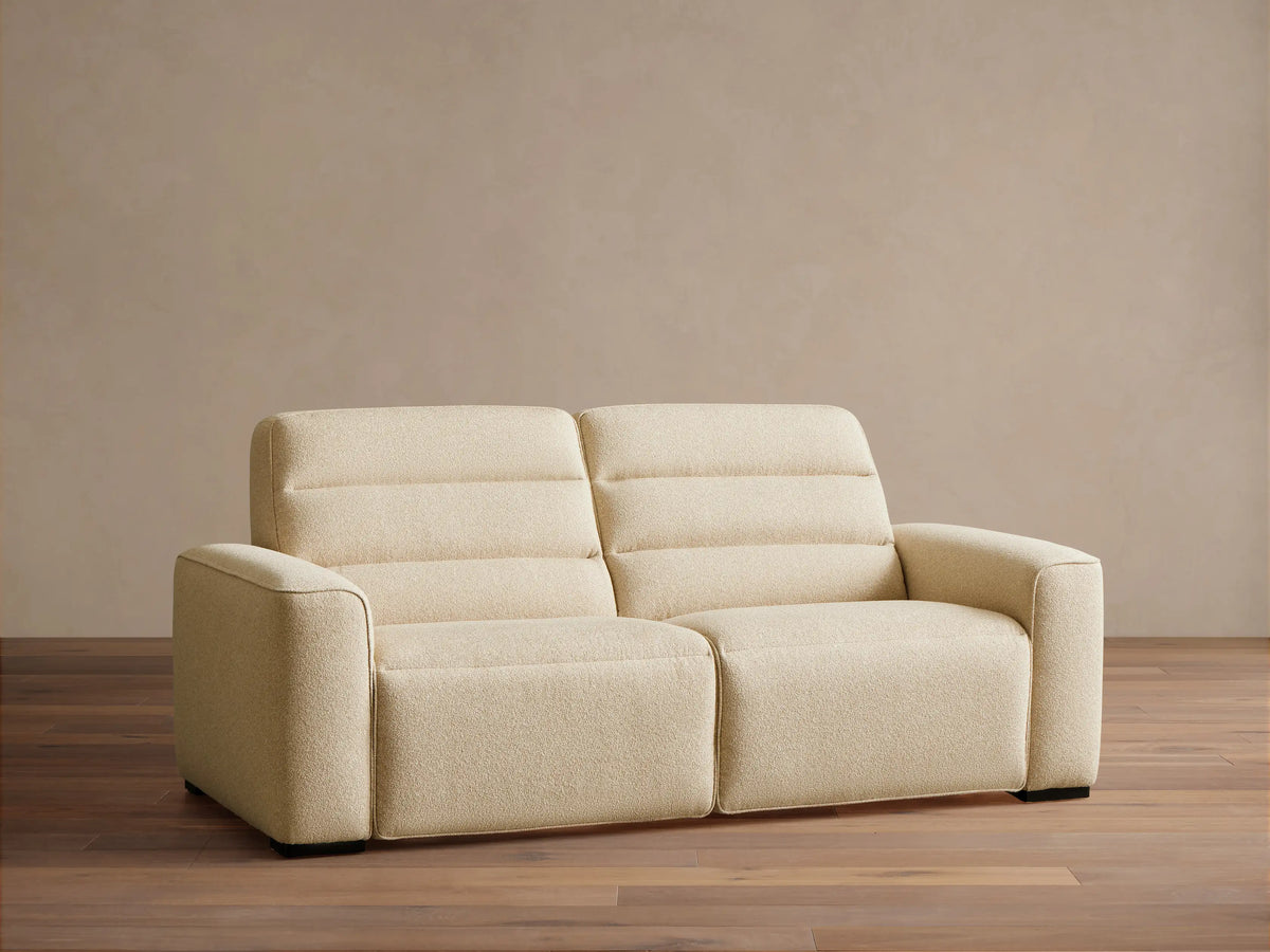 Front view of the cream Borough Two-Piece Motion Sofa, a two-seater with horizontally stitched back cushions and wide armrests.