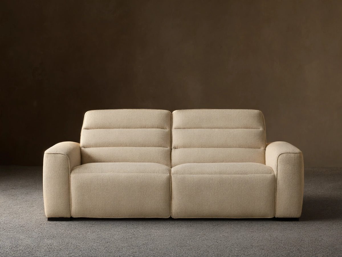 Front view of the cream Borough Two-Piece Motion Sofa, a two-seater with horizontally stitched back cushions and wide armrests.