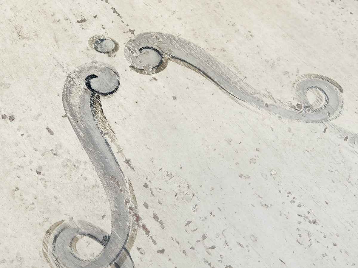 Close-up of Biancca Dining Table's distressed antique white surface with hand-painted antique grey floral scroll design.